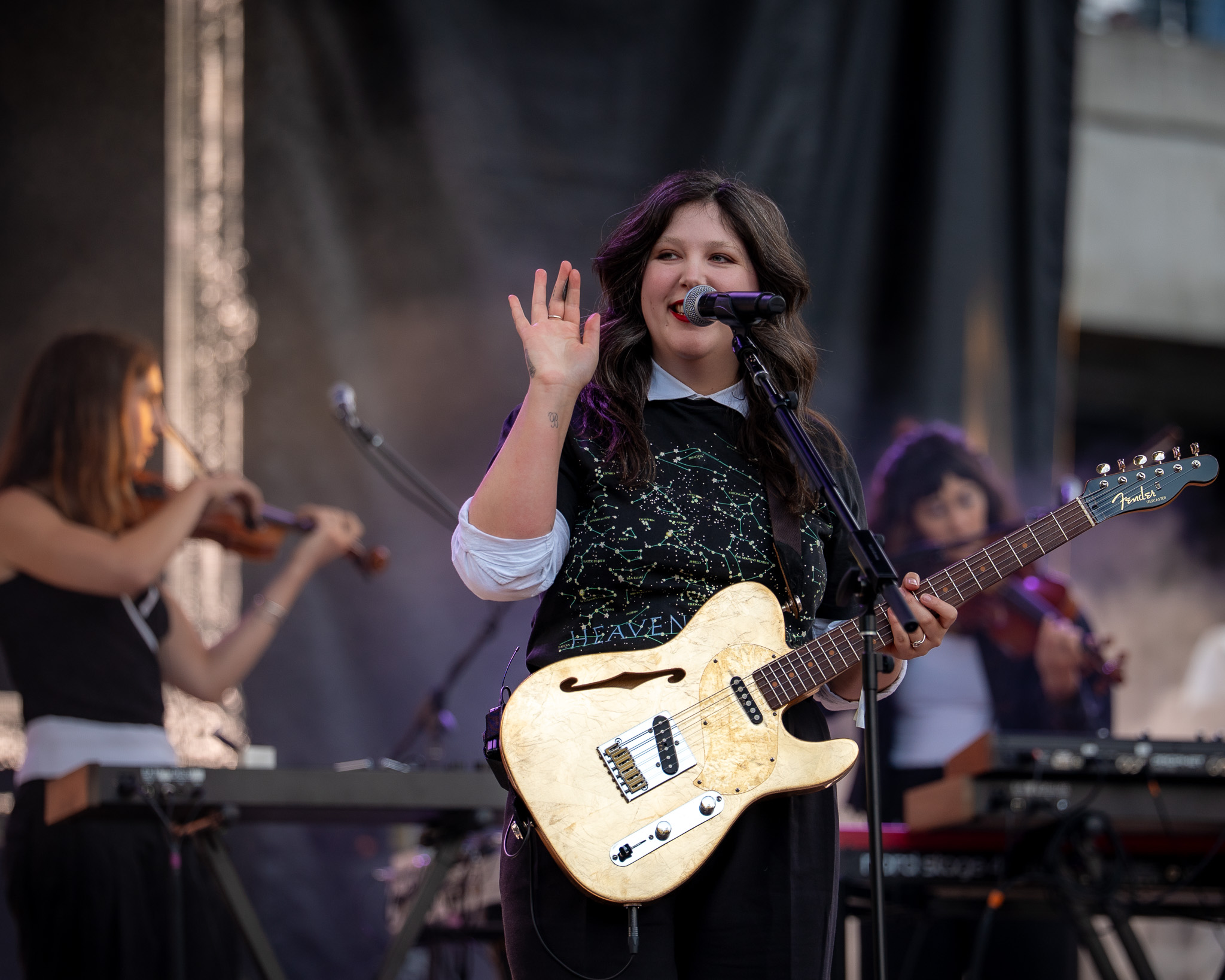 Lucy Dacus smiling with her guitar as string players perform behind her