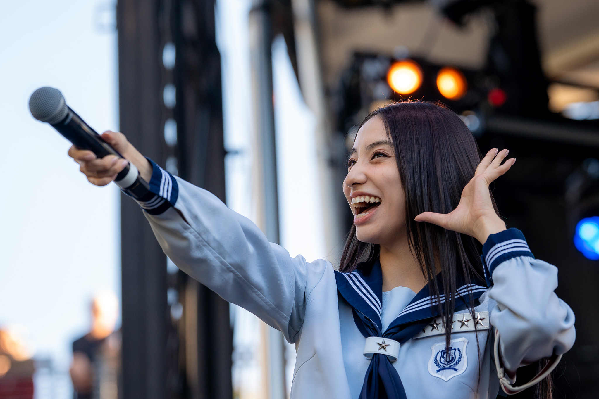 A member of ATARASHII GAKKO! smiling and reaching toward the crowd