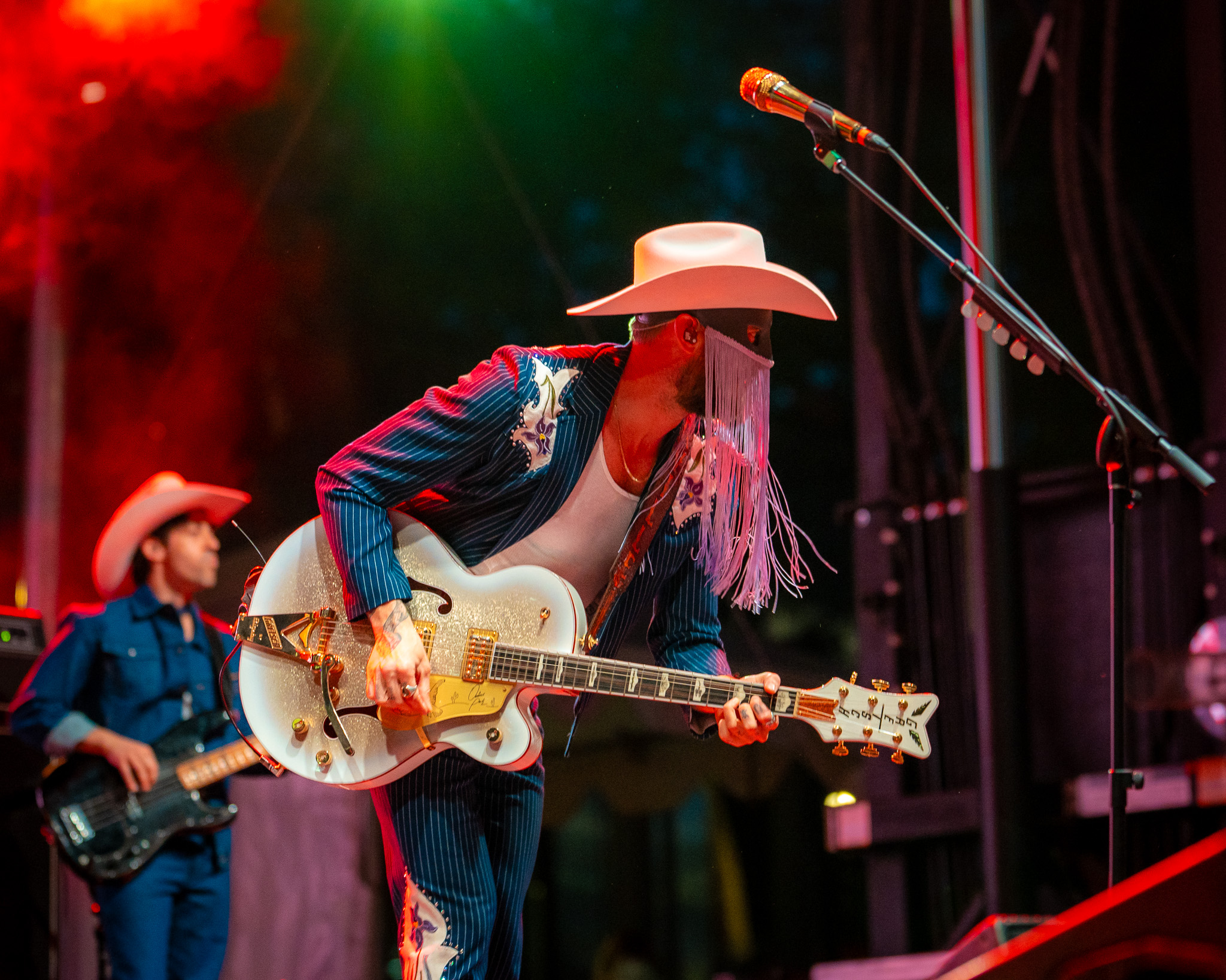 Orville Peck playing guitar beneath red stage light