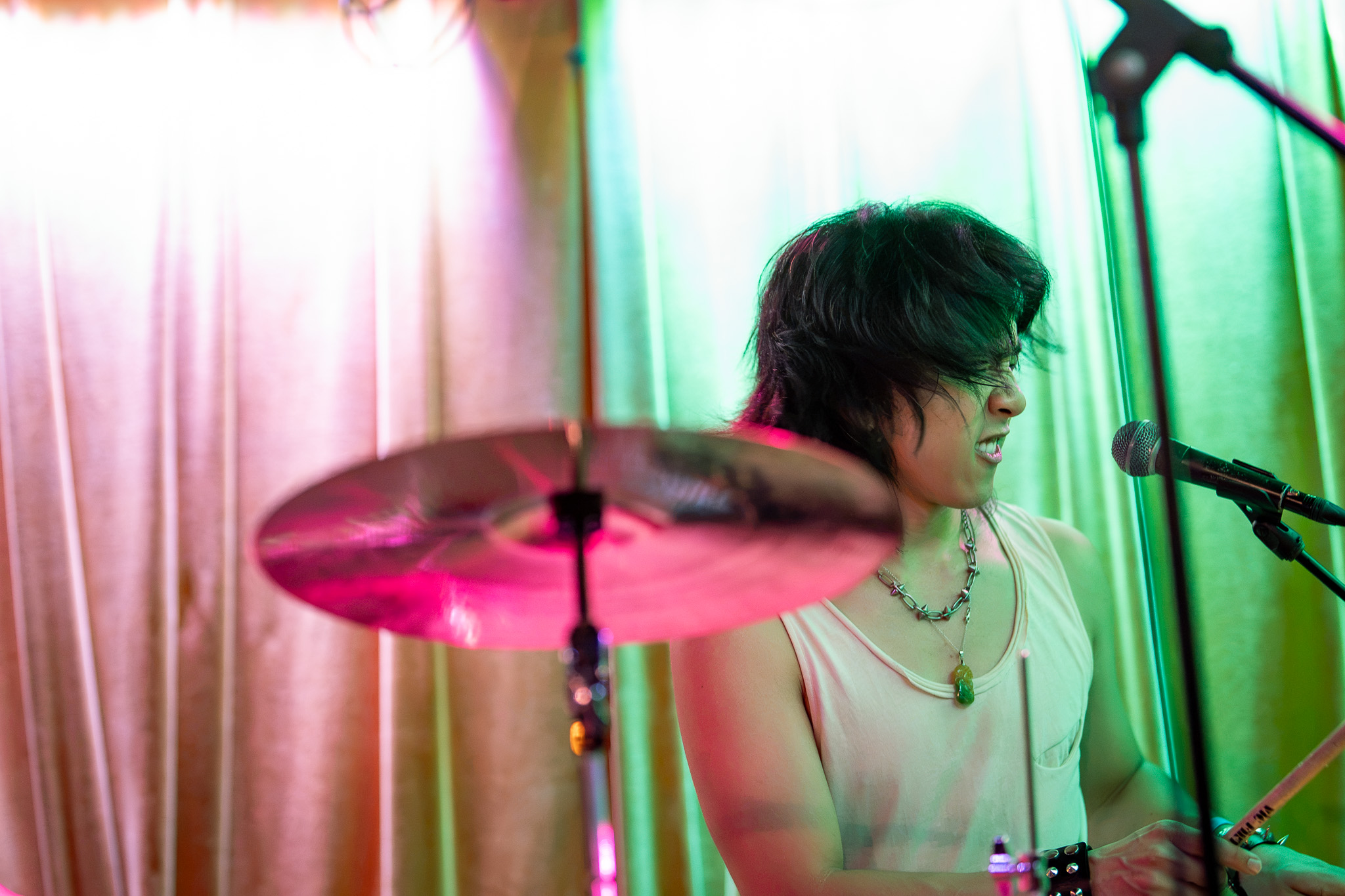 CHANPAN's drummer sings behind a cymbal in pink and green light