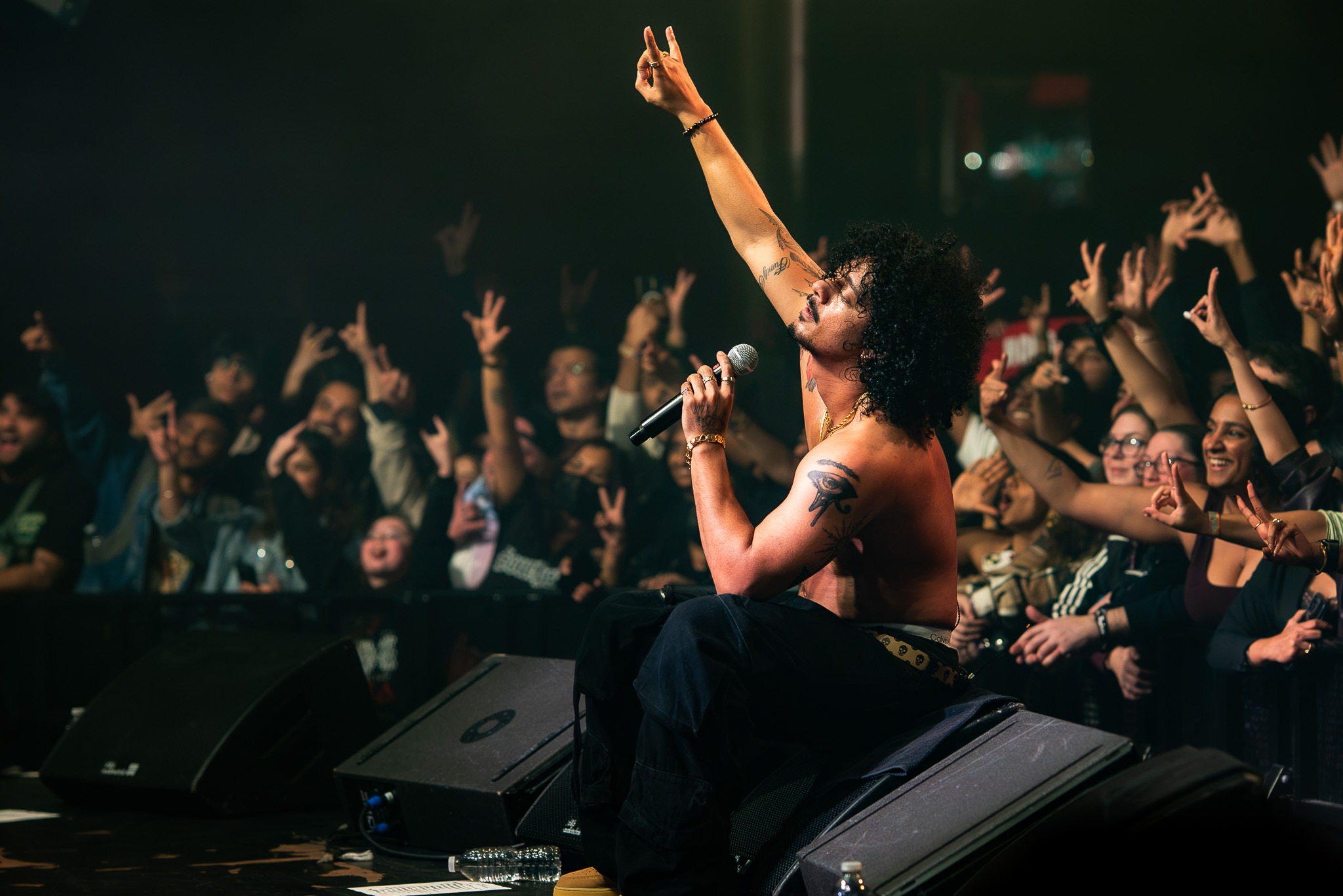 Hanumankind seated at the edge of The Showbox stage with one arm raised above the crowd