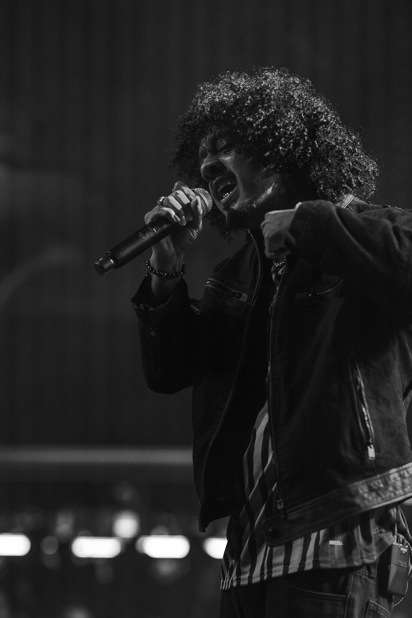 Hanumankind singing in a black jacket under a hard stage light