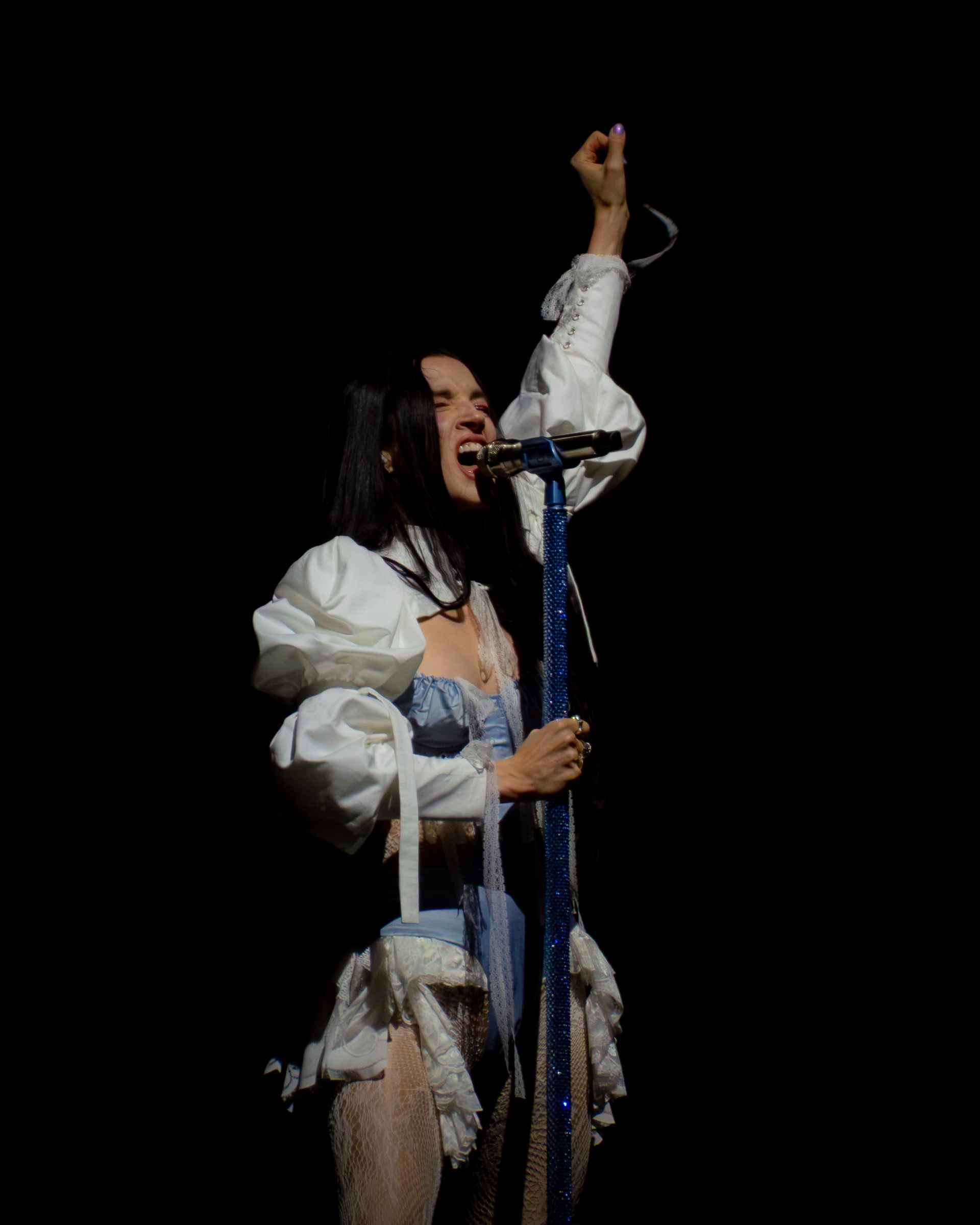 Poppy sings into the crystal microphone stand with one arm raised