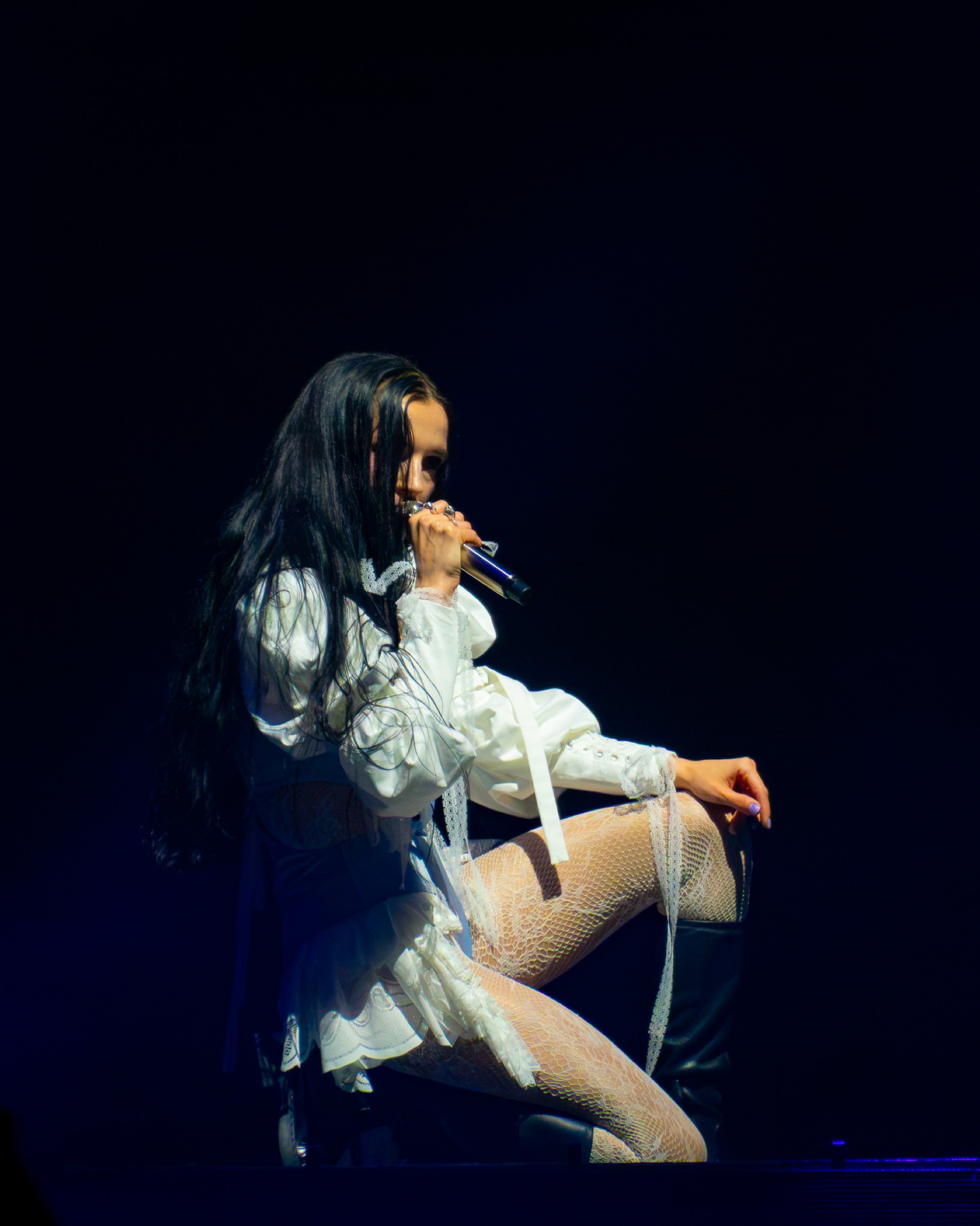 Poppy kneels at the front of the stage with the microphone close to her face