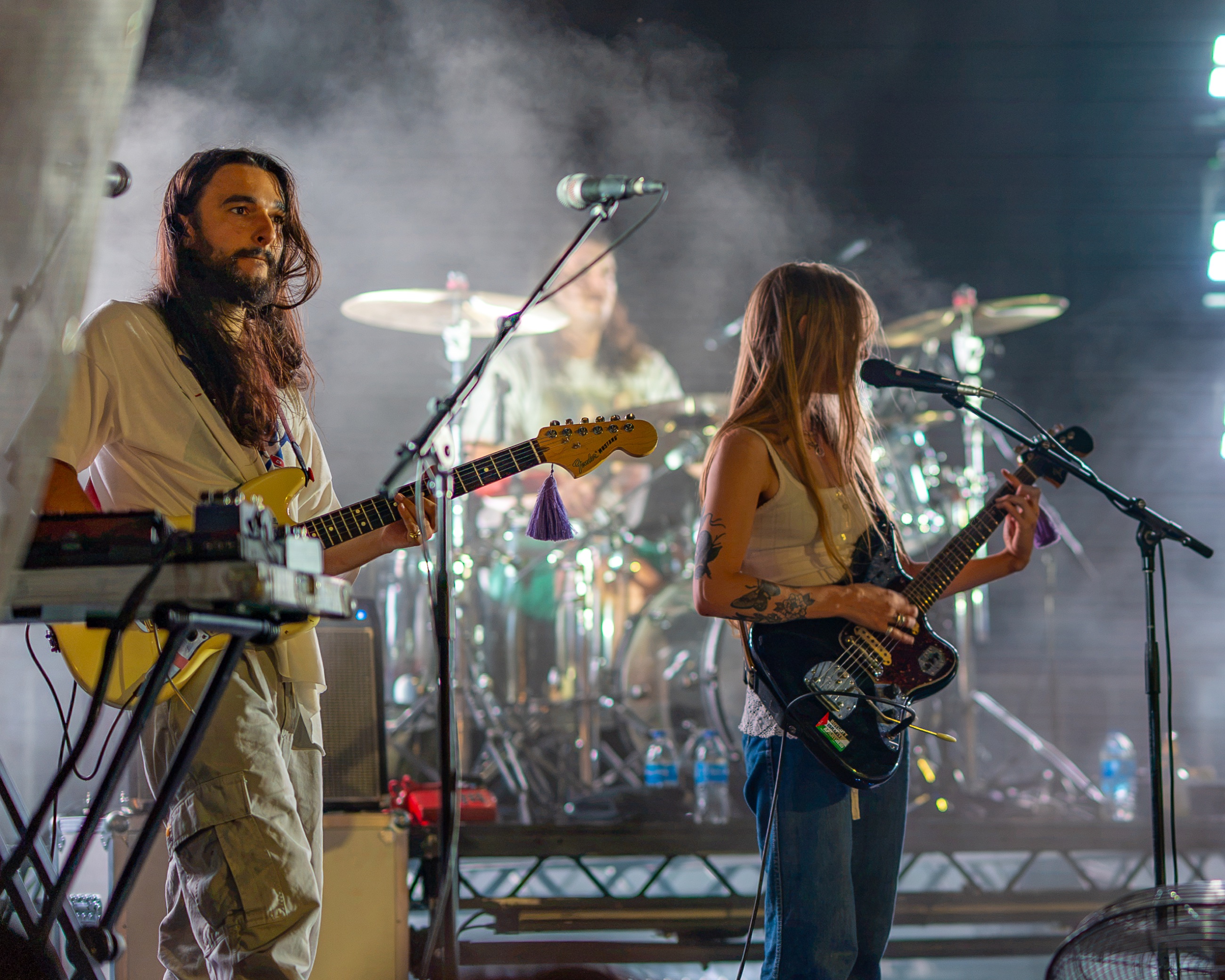 Wet Leg guitarists playing together with the drummer visible through stage smoke