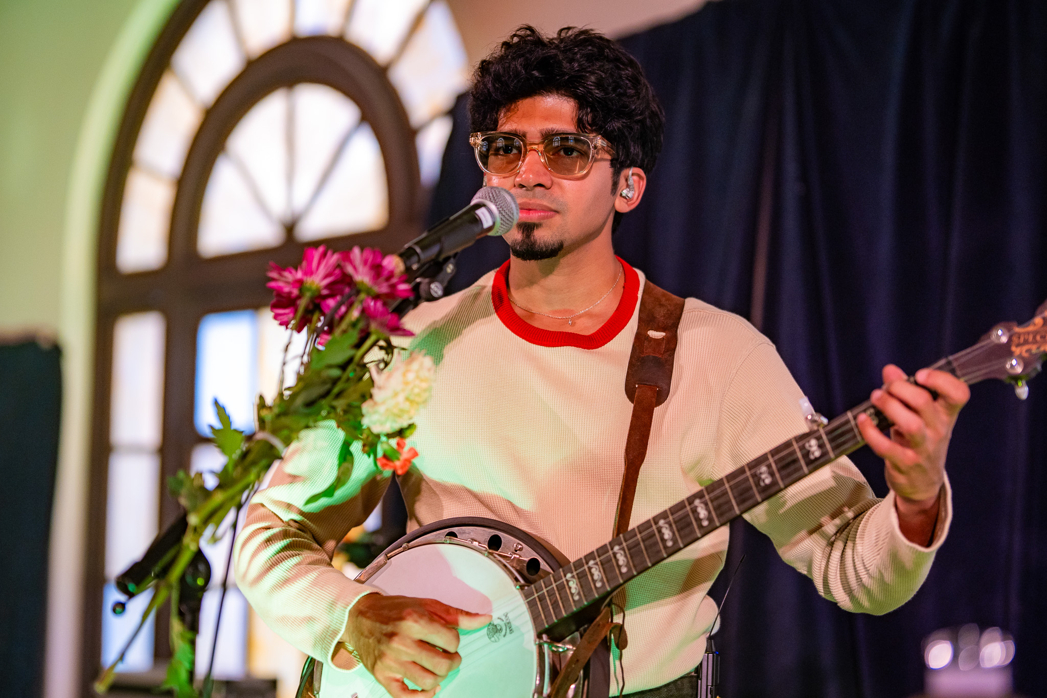 A member of When Chai Met Toast sings while playing banjo at a flower-wrapped microphone