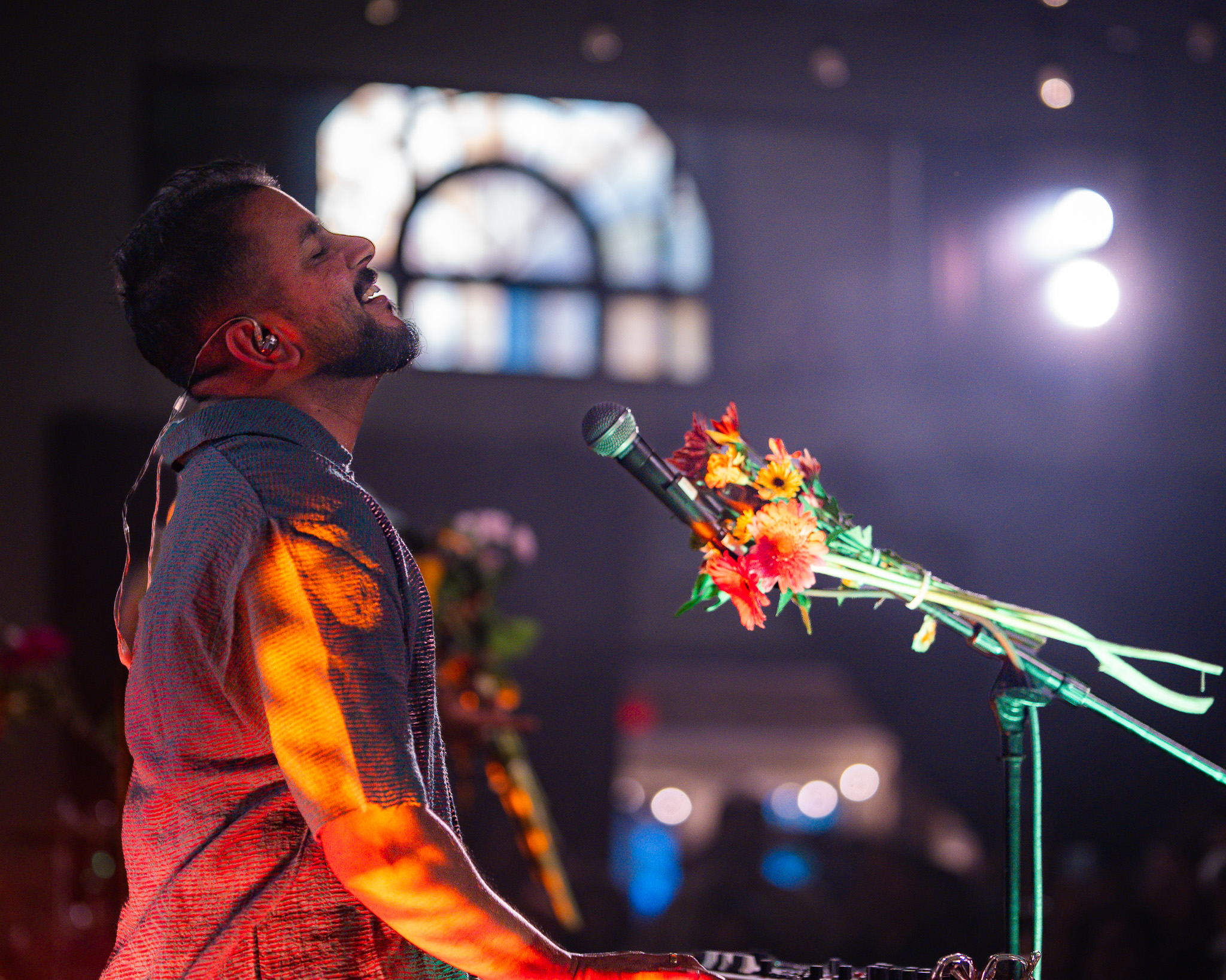 A musician tilts his head back beside a microphone wrapped in flowers
