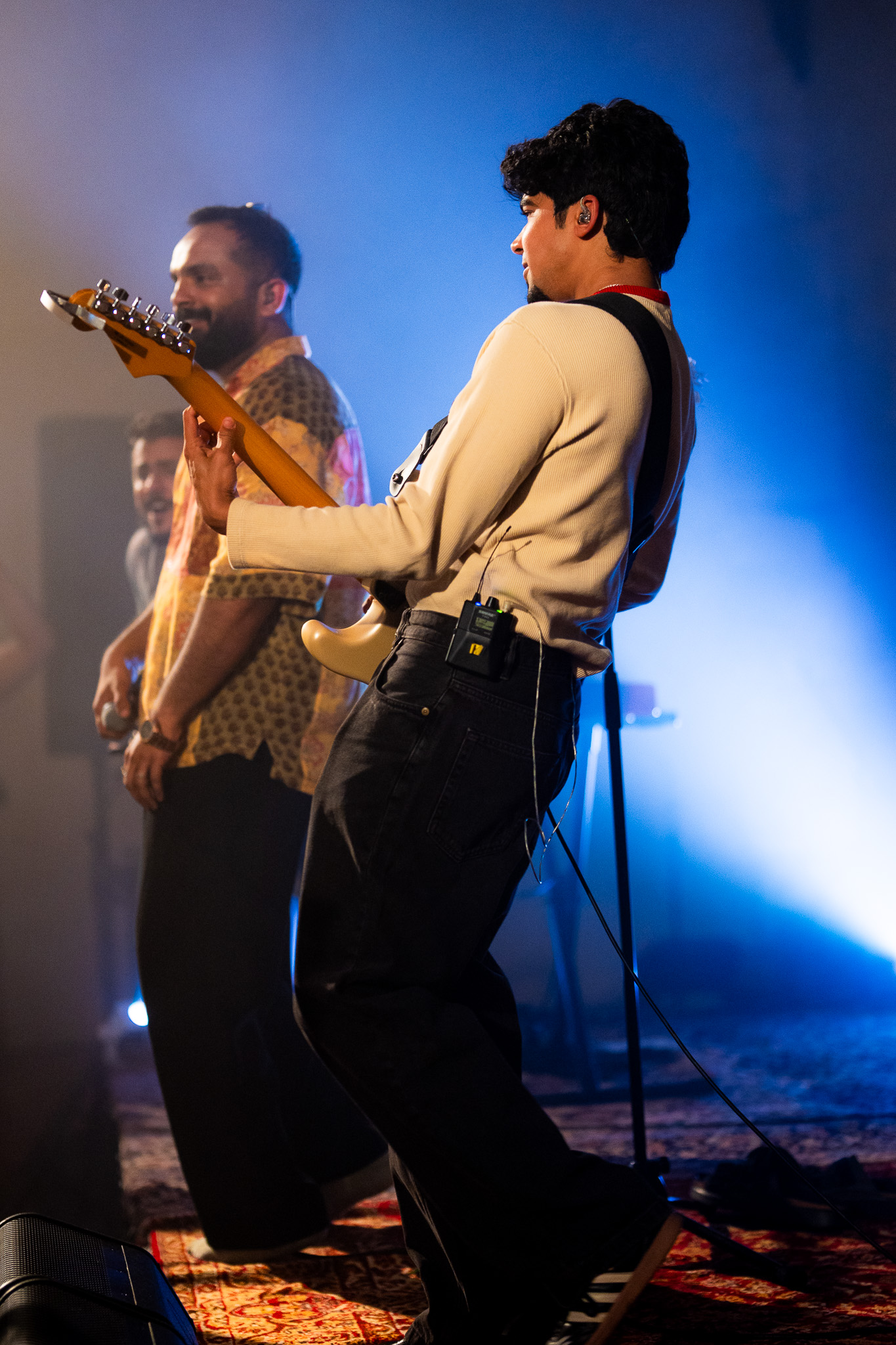 A guitarist leans into the performance as the lead singer watches