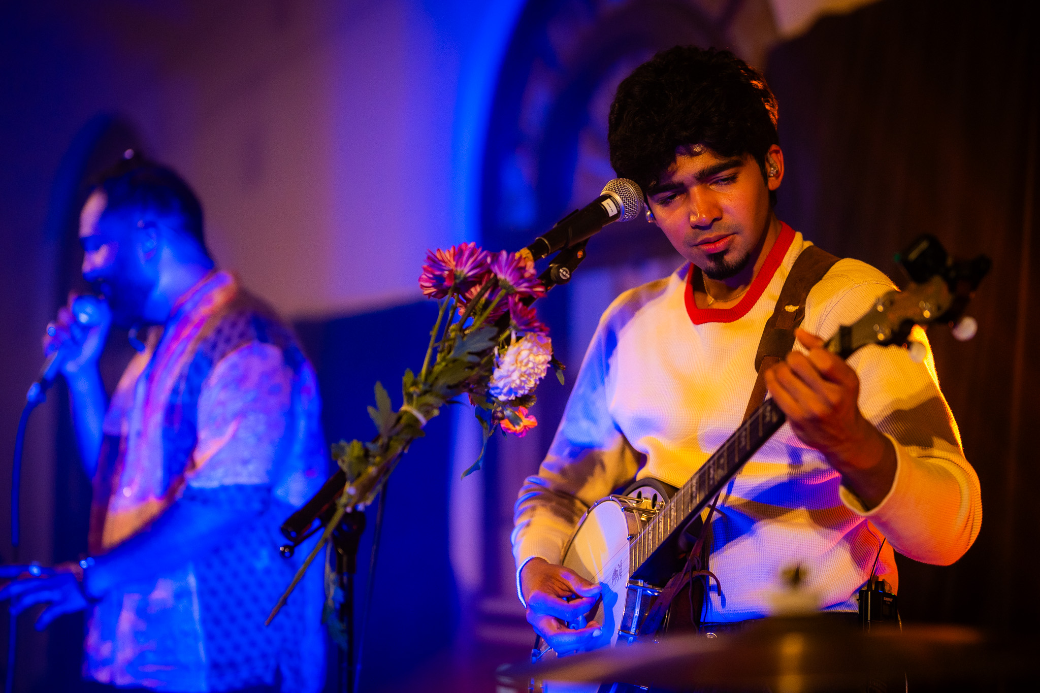 A banjo player performs beside the singer under blue and amber light